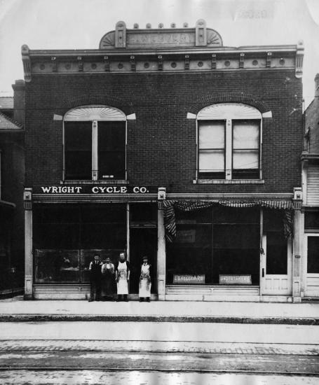 A brick, two-story bulding with a sign on a front facade labeling the building as "The Wright Cycle Co."