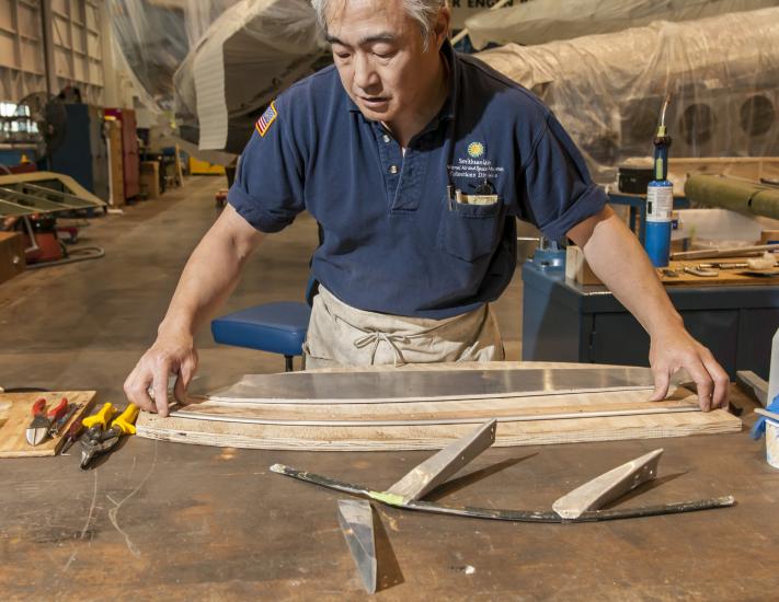 A male staff member of the museum's Collections Department works on restoring part of a World War II era bomber in the museum's restoration hangar.