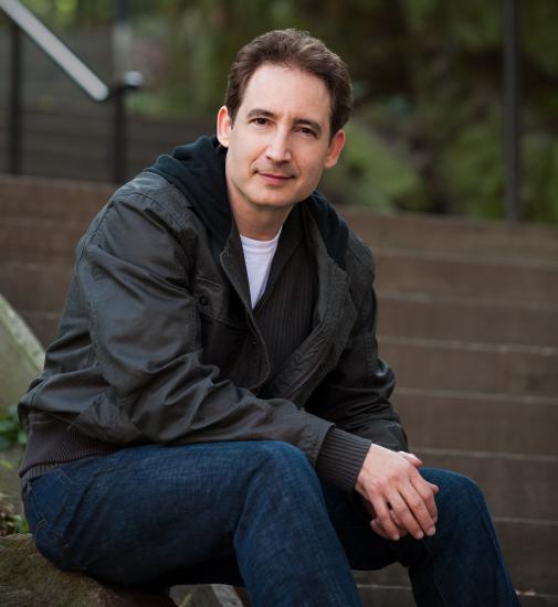 Dr. Brian Greene, a white man, sits as he poses for a portrait.