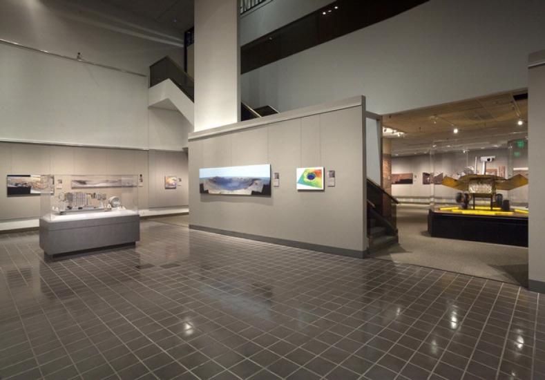 An open area of an exhibit on Mars Rovers with nearby pictures of Mars taken by the Rovers and a small exhibit table.