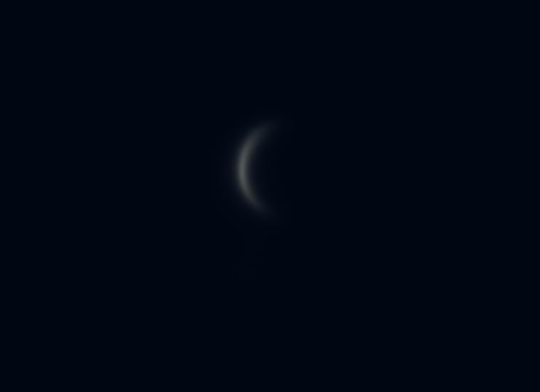 View of Venus in a waxing crescent phase during daytime hours. The crescent is just barely visible and is very thin.