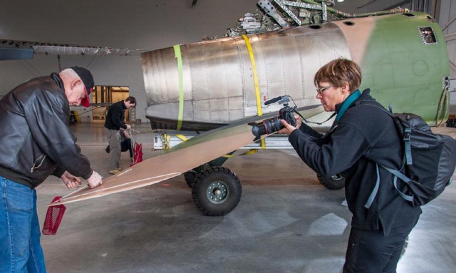 A camerawoman films a white male Museum specialist removing red tags from an aircraft.