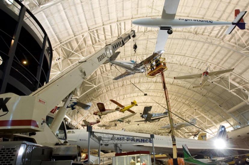 Museum staff members hang a silver monoplane onto the roof of the aircraft hangar at the Steven F. Udvar-Hazy Center.