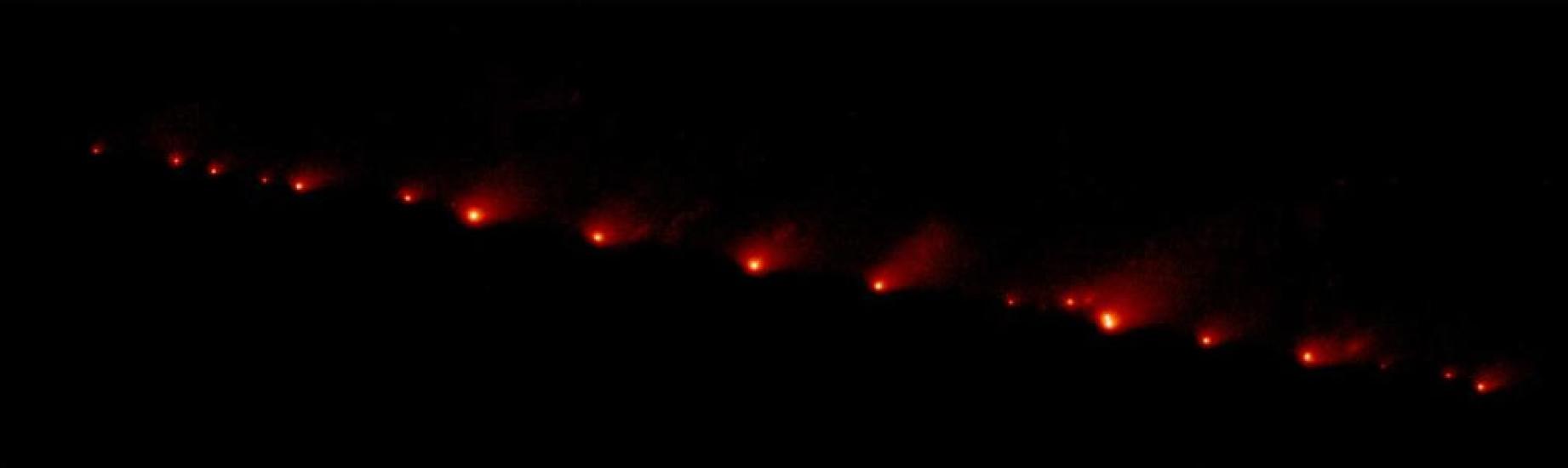 A view of a comet as it soars across space, leaving a red trail of dust behind a lighter red dot.