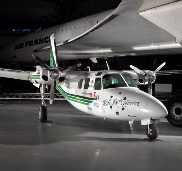 Partial side view of white monoplane with black and green stripes lining the side of the plane. The monoplane has two twin engines, one on each wing.