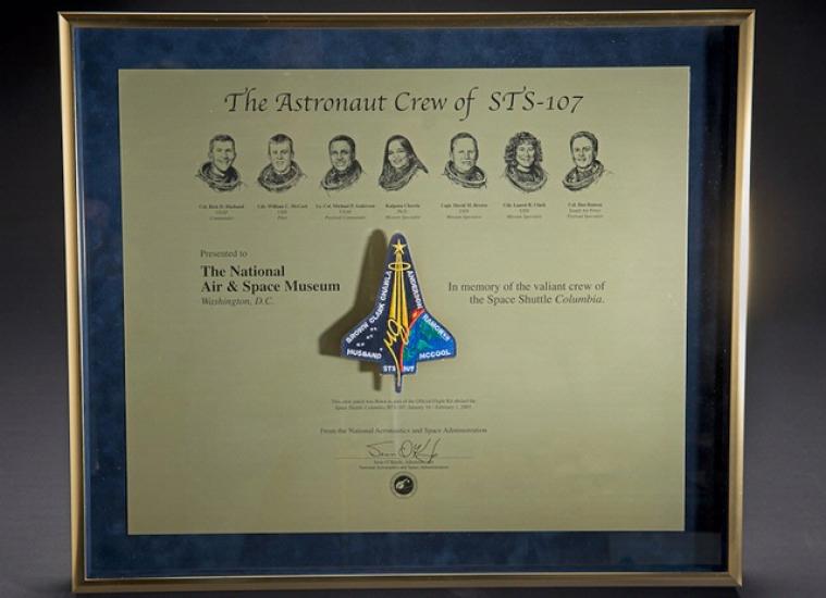 A plaque honoring the members onboard the Space Shuttle Columbia during the STS-107 disaster with their faces and a depiction of the shuttle engraved into the plaque.