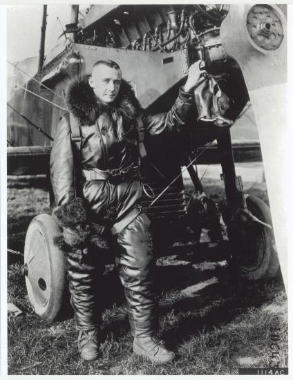 Lt. John Macready, a white man, stands in aviator gear next to an aircraft.