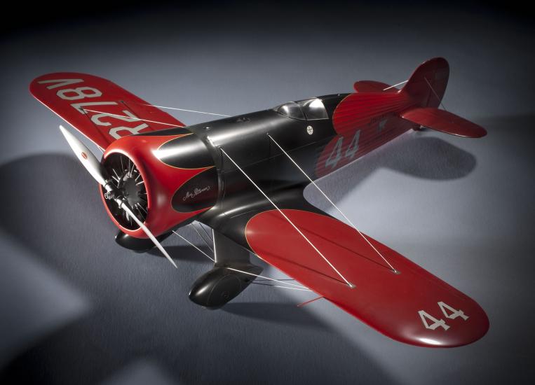 Model of a red and silver-colored monoplane with one engine. Number 44 is painted on the left wing and behind the cockpit of the plane.