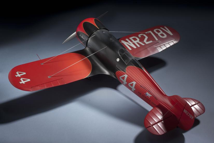 Top-facing view of a red and silver-colored monoplane model with one engine. The number 44 is painted on the left wing and behind the fuselage. Registration number NR278V is painted on top of the right wing.