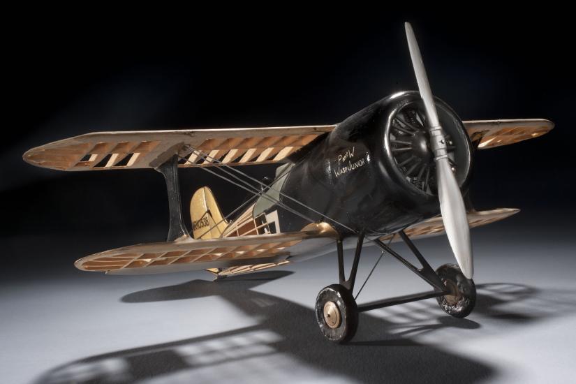 Front-facing view of wooden and black-colored metal biplane model with one engine.