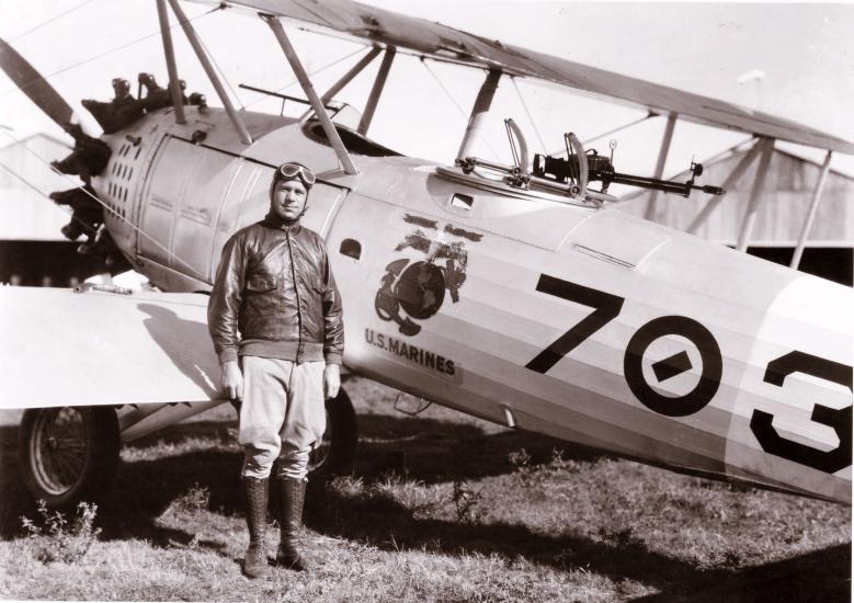 C. Frank Schilt, a white male pilot, stands next to an aircraft wearing aviator gear.