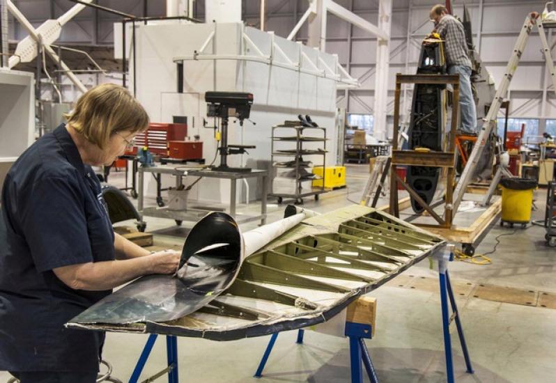 Two museum specialists perform conservation work on a blue military monoplane inside the Museum's restoration hangar.