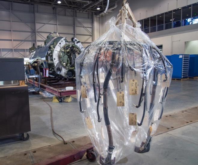 A part of the ignition system of a military aircraft is hanging above the ground in a plastic layer.