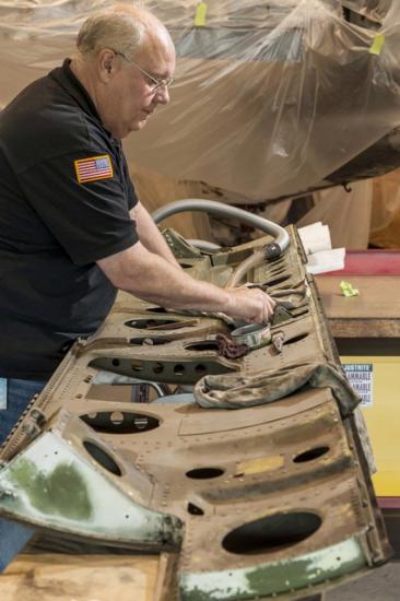 A museum specialist works on cleaning a door of a military monoplane.