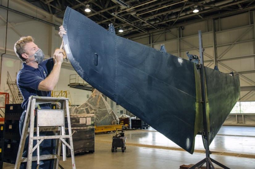 A male museum specialist prepares the tail section of a blue military monoplane for painting.