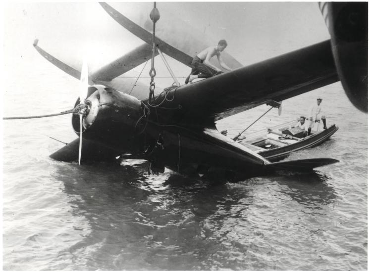 Charles Lindbergh stands atop an capsized aircraft, inspecting it for damage.