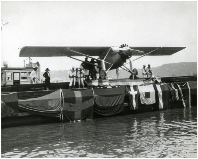 The Spirit of St. Louis sits on a barge as it is exhibited following Charles Lindbergh's record-breaking transcontinental flight. Flags are hung across the side of the barge.