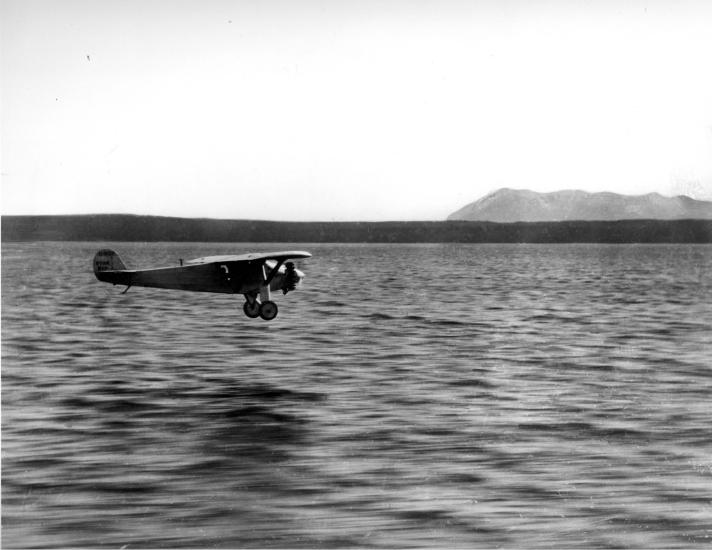 The Spirit of St. Louis, a monoplane with one engine flown by Charles Lindbergh, flies over a body of water.