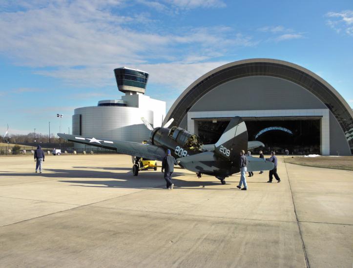 A group museum specialists work to move a gray and black monoplane into its permanent display spot inside the Museum's Steven F. Udvar-Hazy Center.