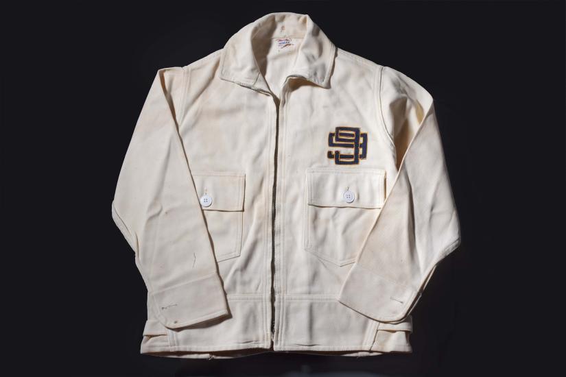 A white jacket intended for flight with a logo of two number nines interlocking on the left chest. The jacket features two pockets on the torso with one button each.