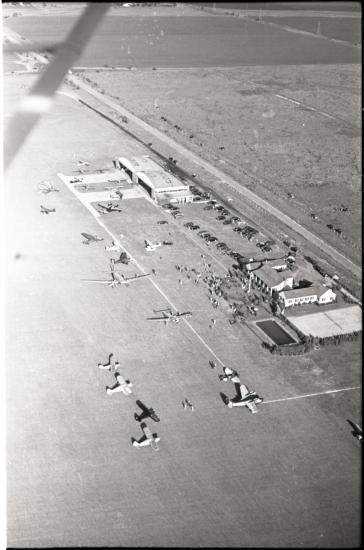 View of an aviation-focused country club from an aircraft. Planes are scattered near two buildings next to a road.