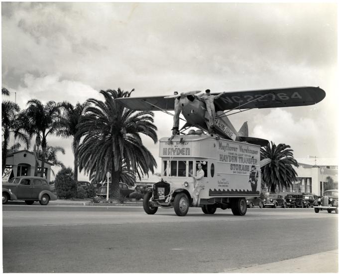 A Piper Cub J-4A, a monoplane with one engine, is displayed on a truck as part of an advertisement.