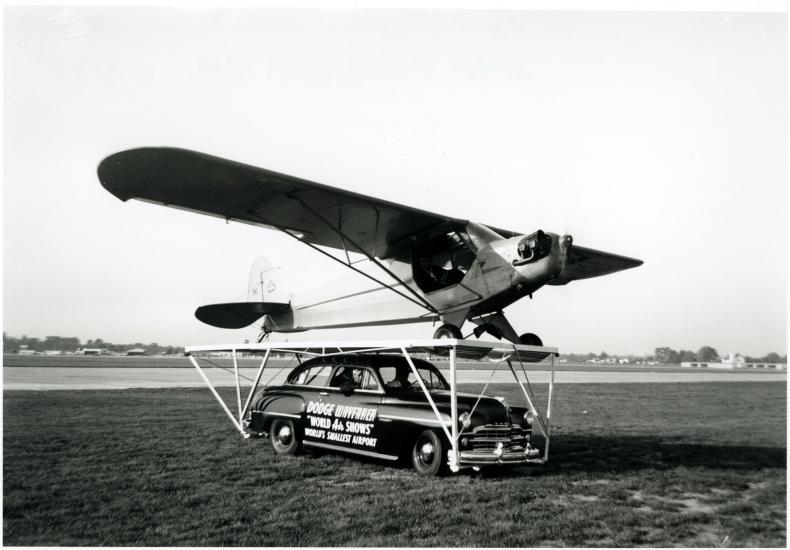 A Piper Cub, a monoplane with one engine, is placed on top of a car prior to performing a stunt.