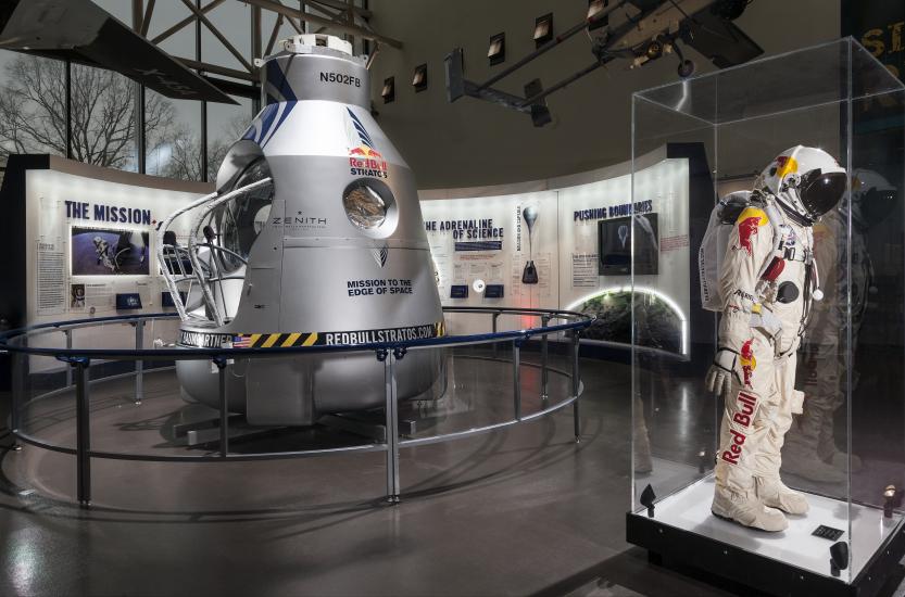 Side view of an exhibit about a Red Bull-sponsored free falling mission from the edge of space. A high-altitude pressure suit is seen in front of the silver-colored opened capsule used to freefall.