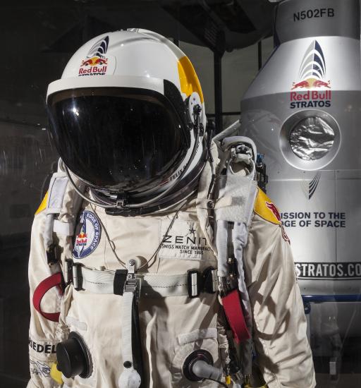 Close up of a high-altitude pressure suit used in a free-fall mission sponsored by Red Bull. The suit is a light-brown color and contains multiple tubes for life support. The helmet features a black sun visor.