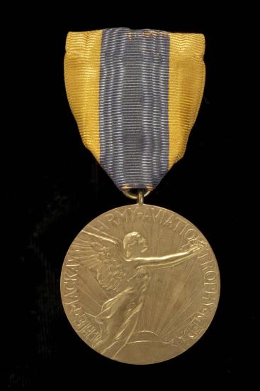 Front of aviation medal. Medallion features an etching of a person with wings in flight as well as the name of the trophy. Suspended using yellow and black fabric.