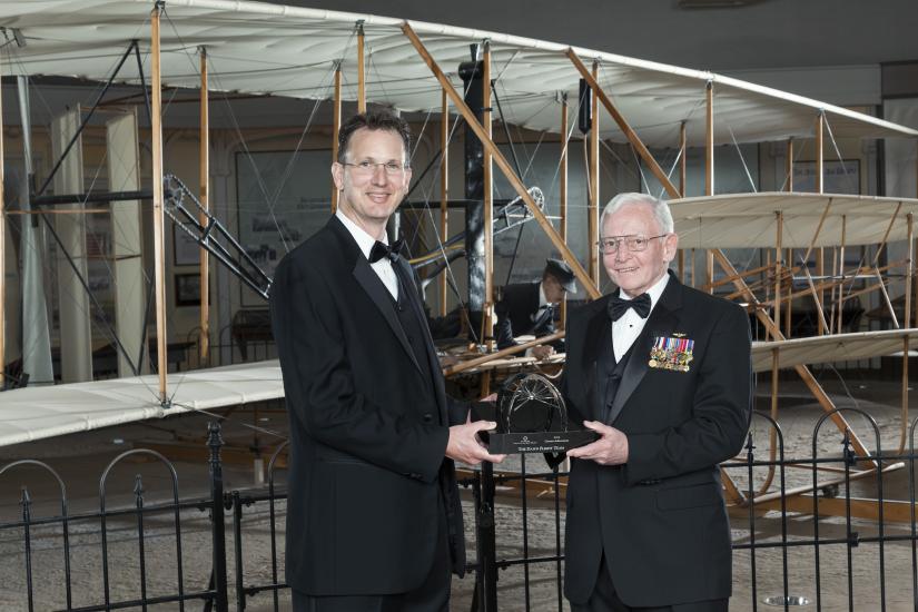 Two white men hold a trophy which was presented at the Museum.