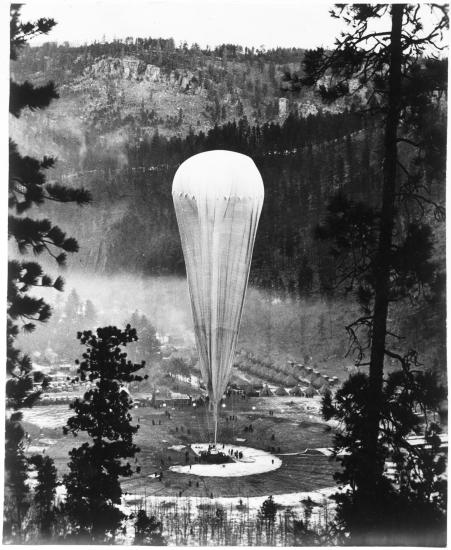 A tall air balloon sits on land in a forest clearing.