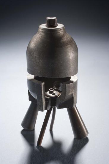 Metal rocket motor with four leg-like tubes below a cylinder-shaped combustion chamber. Small cutaway revealing the interior of the chamber. A second cutaway opens the halves of the motor.