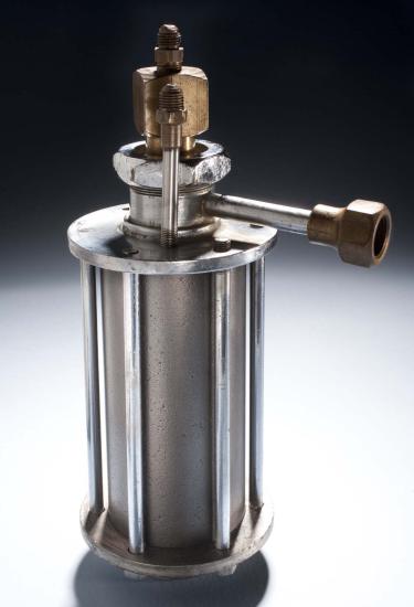 Metal rocket motor with cylinder base surrounded by metal support beams, which is attached to a bottom motor with tubes leading to two brass-colored nozzle halves and a third tube leading to a brass-colored horizontal ring.