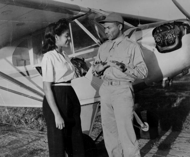 Two African American people stand in front of a small aircraft.