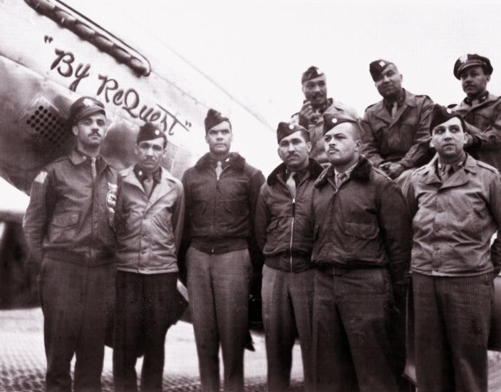 Benjamin O. Davis Jr., an African-American man standing third from the left, poses informally with members of his staff and other Tuskegee Airmen in front of a plane.