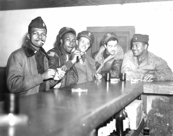 A group of Tuskegee Airmen sit and enjoy drinks and conversation at a bar.