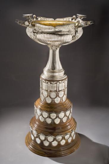 Aviation trophy with wooden tri-base holding military achievements on tiny plaques. The topper features four versions of Nike, Greek goddess of victory, holding a depiction of the Wright Military Flyer.