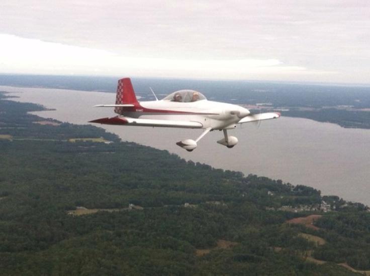 Side view of white and red monoplane with one engine and fixed landing gear. Monoplane is in flight.