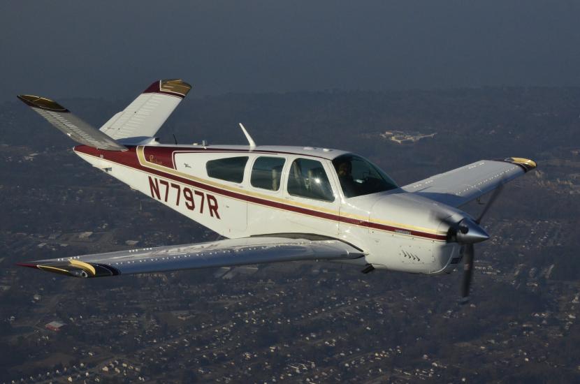 Side view of white and red monoplane in flight. Monoplane has one engine and registration number "N7797R" written in red on the back half of the fuselage.