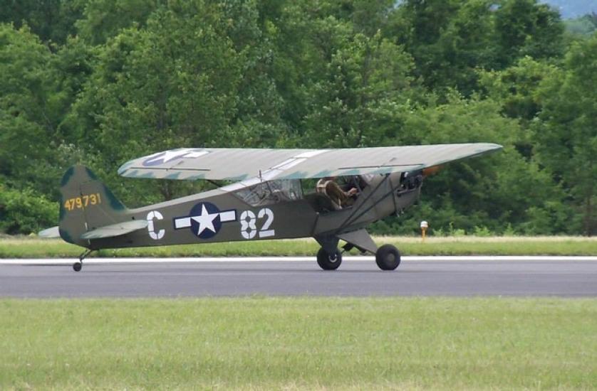 Side view of gray and green military monoplane with one engine.The letter "C" and number "82" are painted in white paint on the sides of a blue and white star emblem.