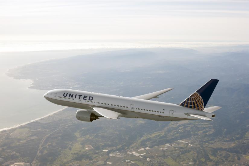 Side view of Boeing 777, a white commercial jet, in flight. The plane features white, blue, and yellow United Airlines livery.