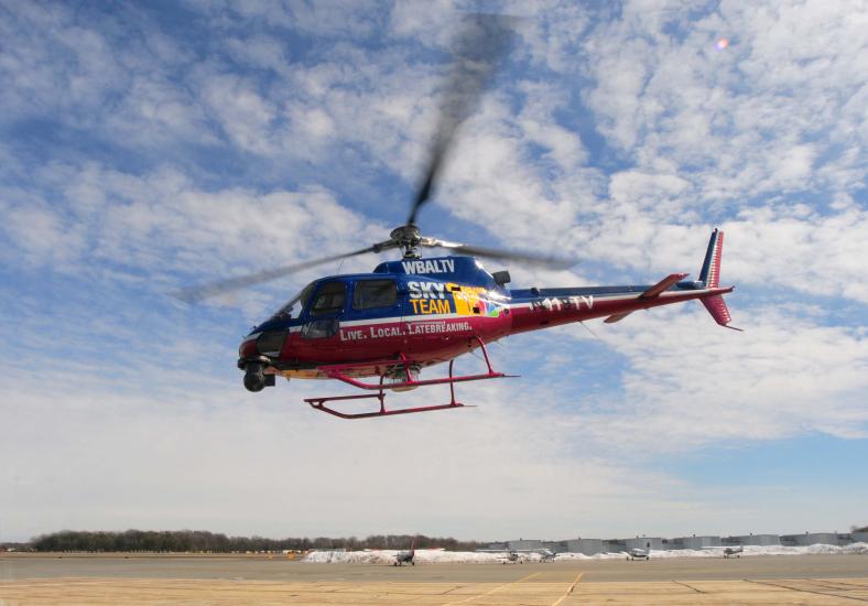 Side view of blue and red helicopter with three-blade top propellor. Helicopter is in flight.