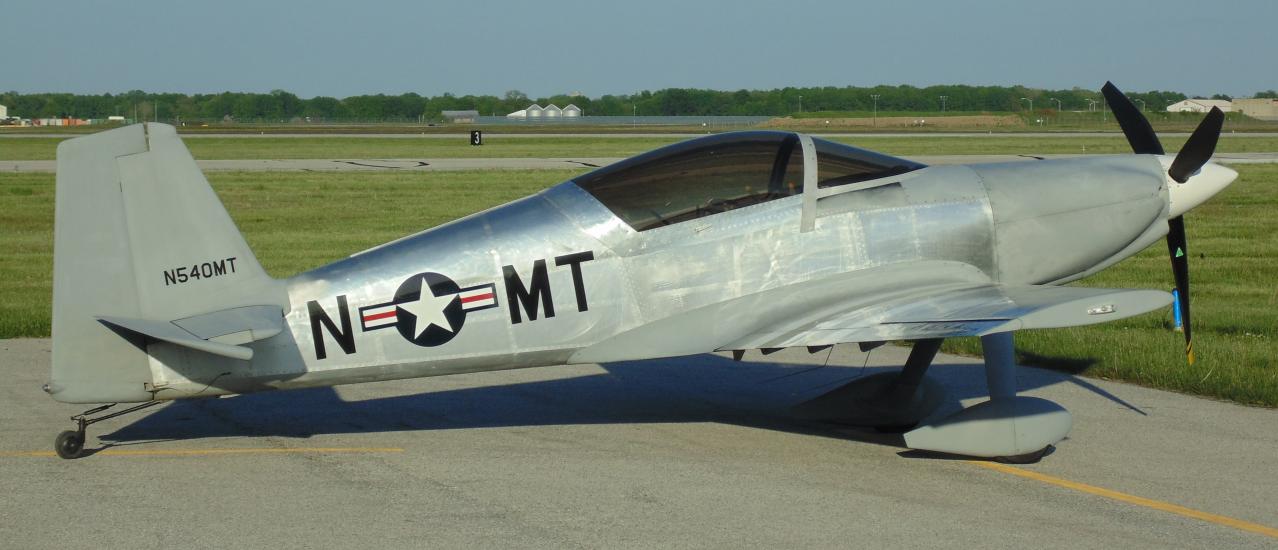 Side view of silver monoplane with one engine and fixed landing gear.