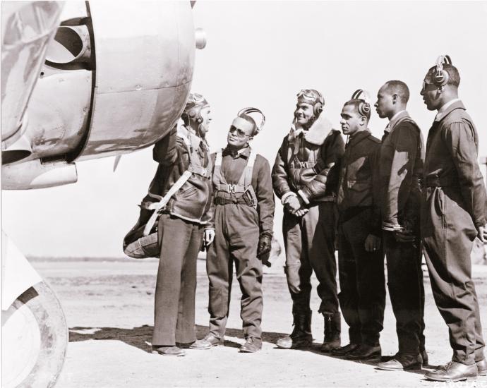 Five pilots who recently received their new status as Tuskegee pilots stand with another person next to a trainer aircraft.