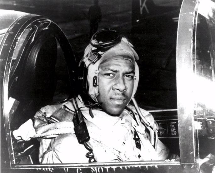 Jesse L. Brown, an African-American pilot who was part of the U.S. Navy, sits in the cockpit of an aircraft. He is wearing aviator gear.