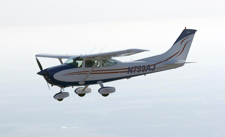 Side view of white monoplane in flight. Monoplane has one engine, fixed landing gear, and black and red accents. Registration number "N759AJ" is painted in black near the rear of the fuselage.