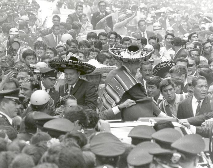 The three Apollo 11 astronauts (Neil Armstrong, Edwin "Buzz" Aldrin, Jr., and Michael Collins) are wearing sombreros and ponchos. They are surrounded by thousands of people in Mexico City, Mexico.