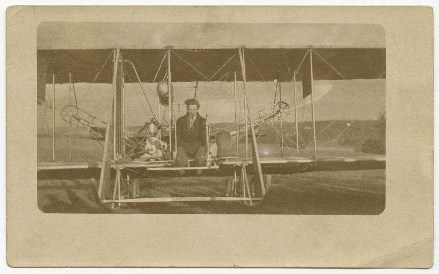 Harry Bingham Brown, a white male, sits at the cockpit of a Wright biplane.