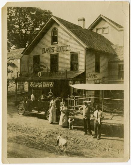 Harry Bingham Brown, a white male pilot, stands outside of a hotel named "Davis' Hotel" with other people.